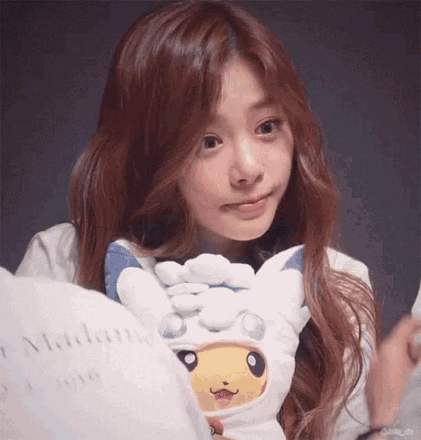 a girl with long red hair is holding a stuffed animal in a pikachu outfit .