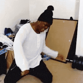 a man wearing a black hat and a white shirt is kneeling down in a room .
