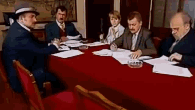 a group of people are sitting around a red table .