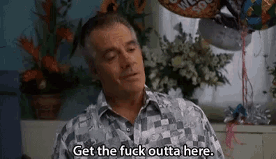 a man is sitting in front of a window with balloons and flowers and says `` get the fuck outta here '' .