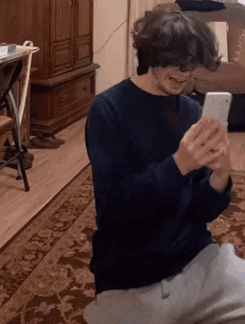 a young man is sitting on the floor looking at his cell phone