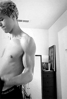 a man without a shirt is standing in front of a mirror in a bedroom .