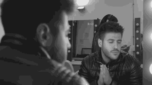 a man in a leather jacket is looking at himself in the mirror