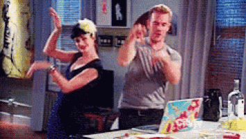 a man and a woman are dancing in front of a table with a laptop on it .