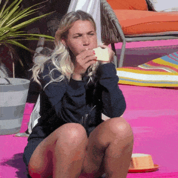 a woman sitting on a pink blanket eating a piece of food