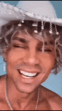 a man with curly hair wearing a cowboy hat is smiling .