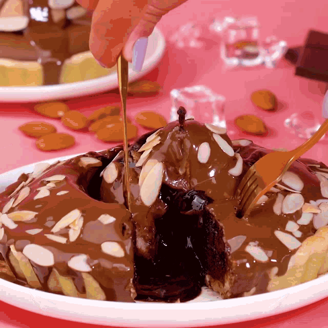 a person pouring chocolate sauce on a chocolate cake with almonds