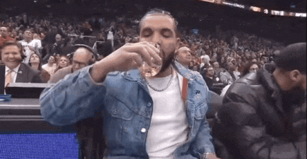 a man in a denim jacket is drinking from a glass in a stadium .
