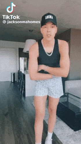 a man wearing a tank top and shorts is standing in a living room with his arms crossed .