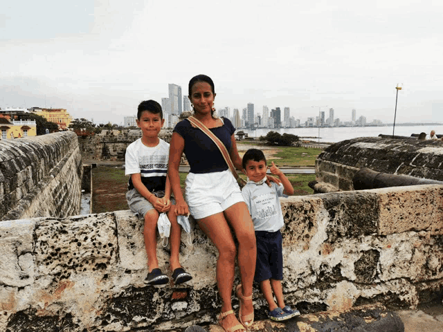 a woman sits on a stone wall with two young boys one of whom is wearing a shirt that says " i love you "