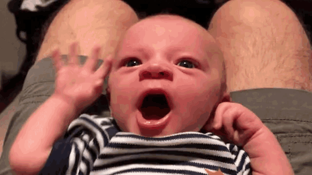 a baby laying on a man 's lap with its mouth open
