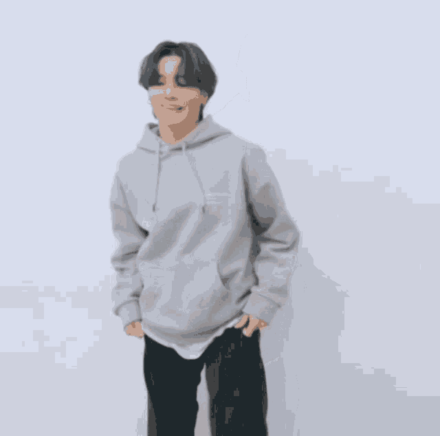 a man wearing a grey hoodie and black pants stands with his hands on his hips