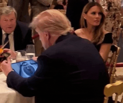 a man in a suit is looking at a tablet while sitting at a table