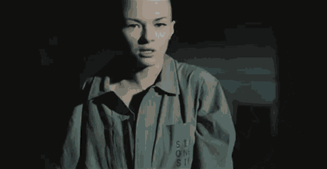 a woman with a bald head is standing in a dark room .
