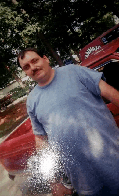 a man in a blue shirt is standing in front of a red truck that says ' nwah ' on the back