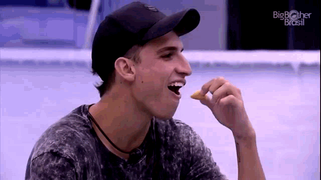 a man wearing a baseball cap is eating a slice of pizza .