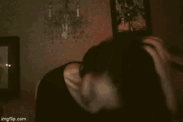 a woman is standing in a dark room with her eyes closed and her hair in her hand .