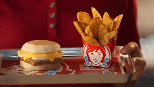 a person is holding a tray with a wendy 's breakfast sandwich and french fries