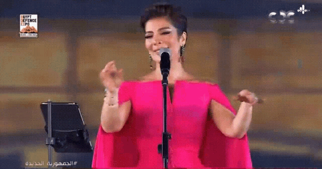 a woman in a pink dress is singing into a microphone with a sign above her that says egypt belongs to us