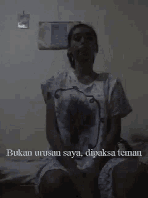 a woman is sitting in a dark room with the words " bukan urusan saya dipaksa teman " above her