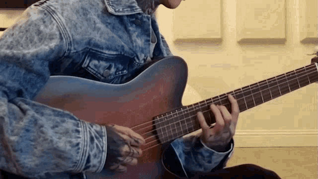 a man in a denim jacket is playing a guitar