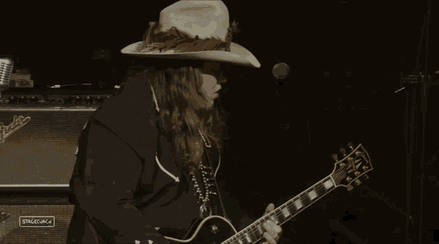 a man wearing a cowboy hat is playing a guitar