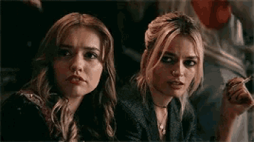 two women are sitting next to each other and one of them is smoking a cigarette