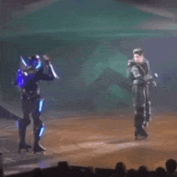 a man in a robot costume is rollerblading on a stage while another man stands behind him .