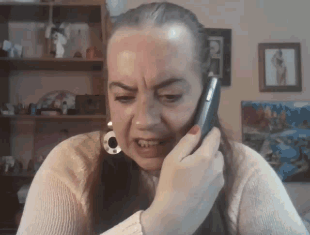 a woman in a white sweater is talking on a cell phone and making a funny face