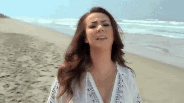 a woman in a white shirt is standing on a beach with her eyes closed