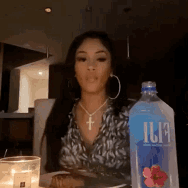 a woman is sitting at a table with a plate of food and a bottle of ilia water .