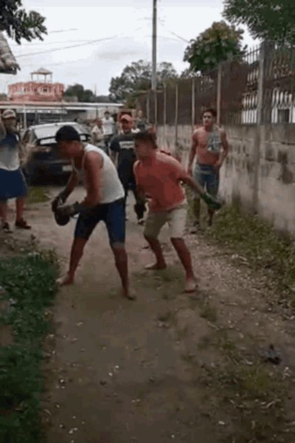 a group of men are standing on a dirt road fighting one another .