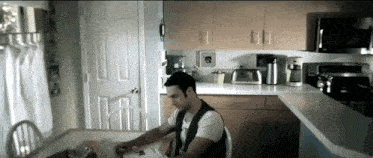 a man sits at a table in a kitchen with a clock on the wall