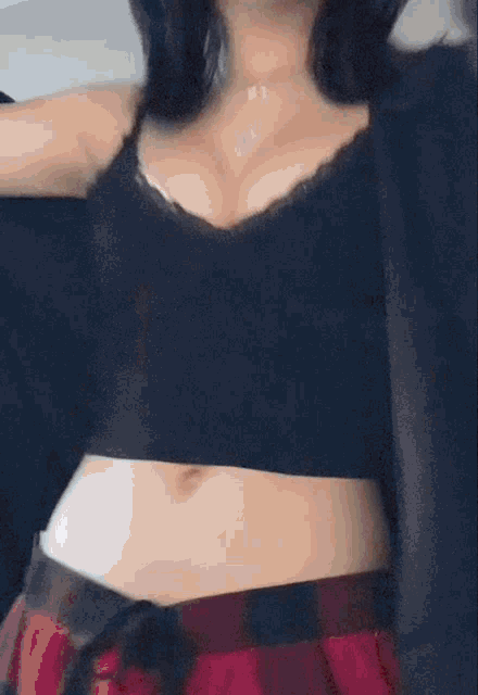 a woman wearing a black crop top and plaid skirt is standing in front of a mirror .