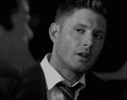 a black and white photo of a man in a suit and tie making a funny face .