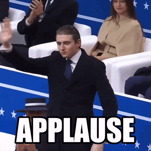 a man in a suit applauds while sitting in a crowd