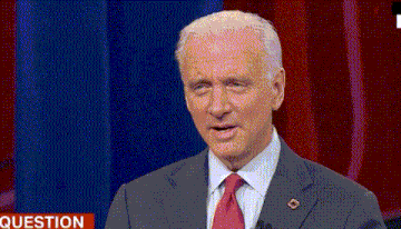 a man in a suit and tie is standing in front of a red curtain and a sign that says question