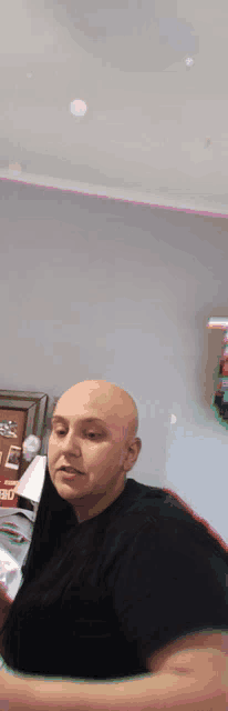 a bald man in a black shirt is standing in front of a christmas tree .