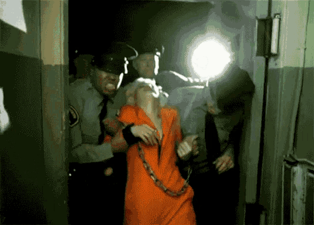 a woman in an orange prison uniform is being led by a group of police officers