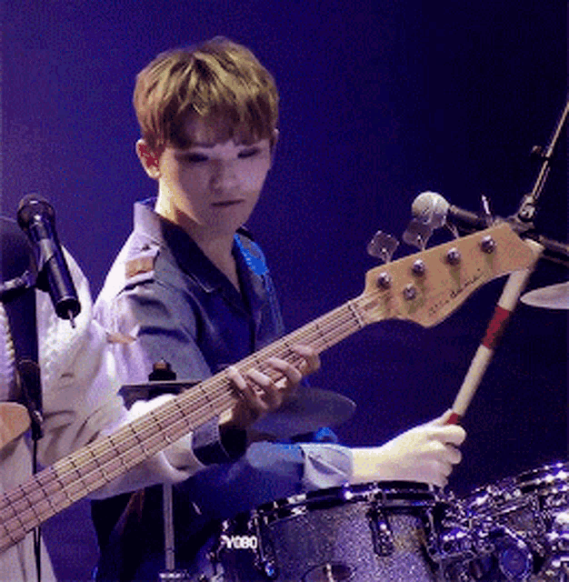 a young man playing a bass guitar in front of a drum set that says ' yamaha ' on it