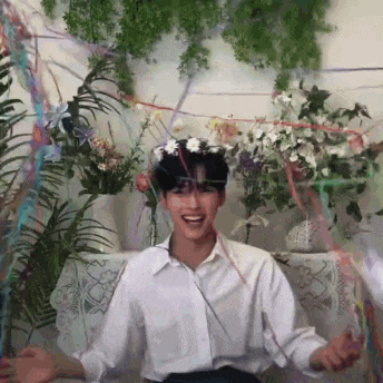 a young man wearing a flower crown is sitting in front of a table with flowers and ribbons .