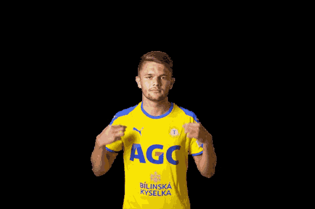 a man wearing a yellow agc jersey holds his arms up