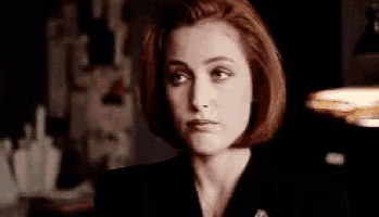 a woman with red hair and a black suit is looking at the camera in a black and white photo .