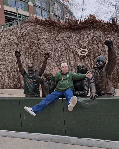 a man in a green bay packers sweatshirt sits on a ledge