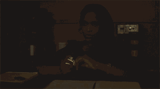 a woman sitting at a desk lighting a lighter in the dark