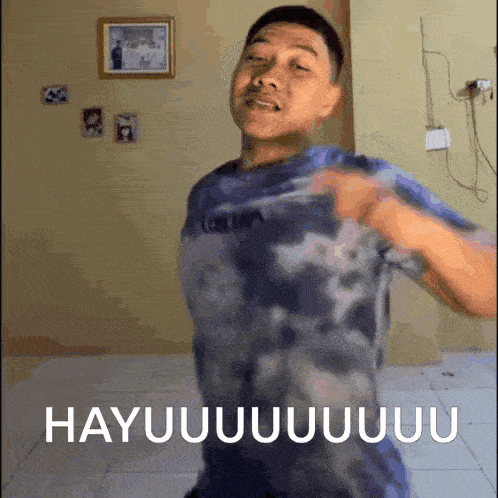 a man in a tie dye shirt is dancing in a room with the words hayuuuuuuuu written on the floor .