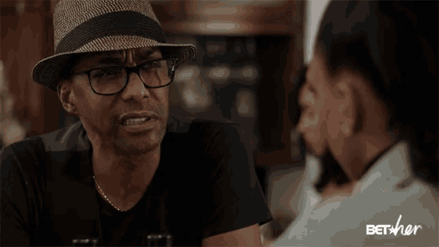 a man in a hat and glasses is talking to a woman and the word thirsty is on the screen