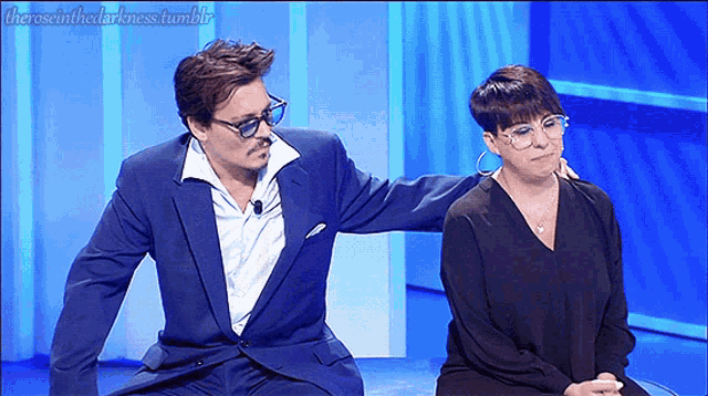a man in a suit is putting his arm around a woman in a black shirt