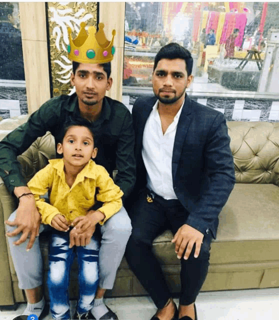 a boy wearing a crown is sitting on a couch with two men