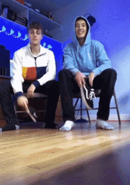 two young men are sitting on chairs and one is wearing a blue hoodie